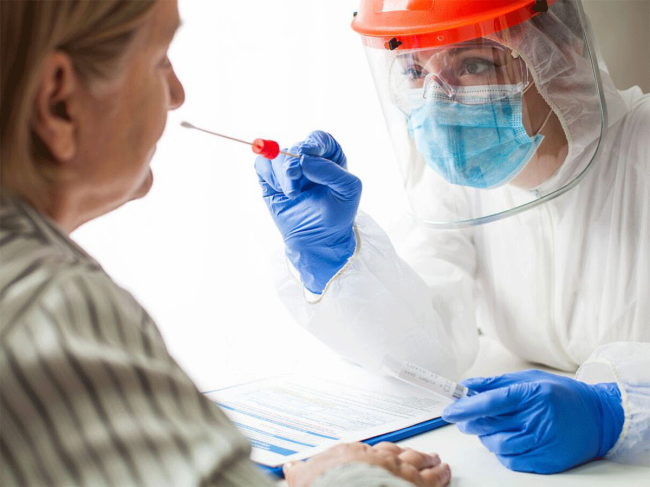 Health care worker in PPE administers nasal swab test