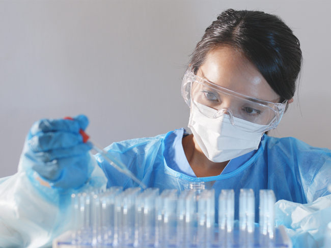 Female researcher wearing mask and safety glasses holding dropper