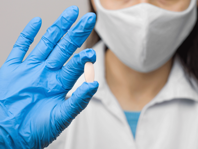 Person wearing mask, glove holding pill