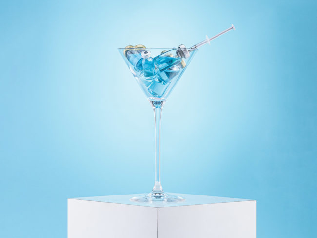 Vaccine vials and syringe in a martini glass.