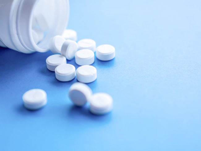 White tablets spilling out of white bottle, blue background