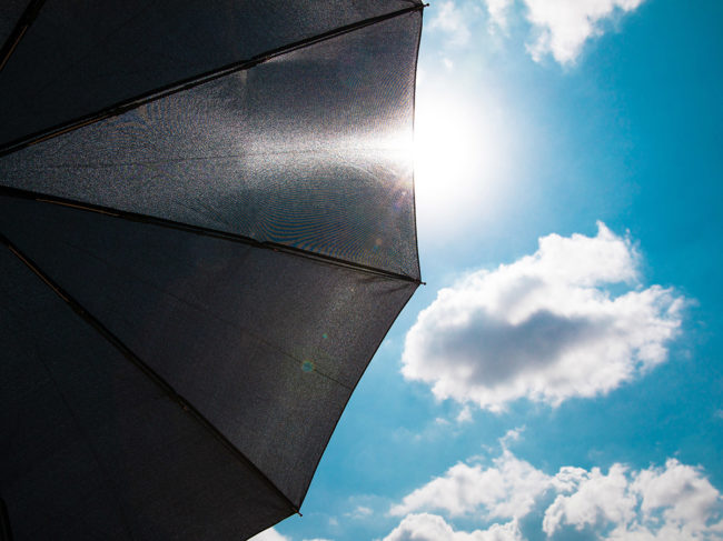 Black umbrella open against blue sky with clouds