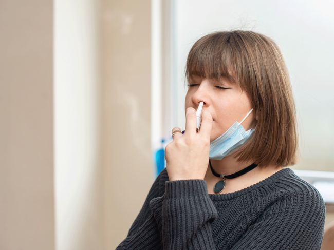 Woman with mask using nasal spray