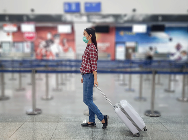 Airport traveler wearing mask, pulling suitcase