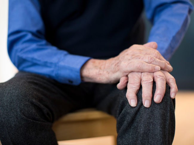 Elderly man rests hands on knee