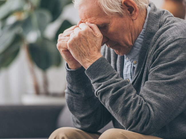 Elderly man with clenched hands holding head